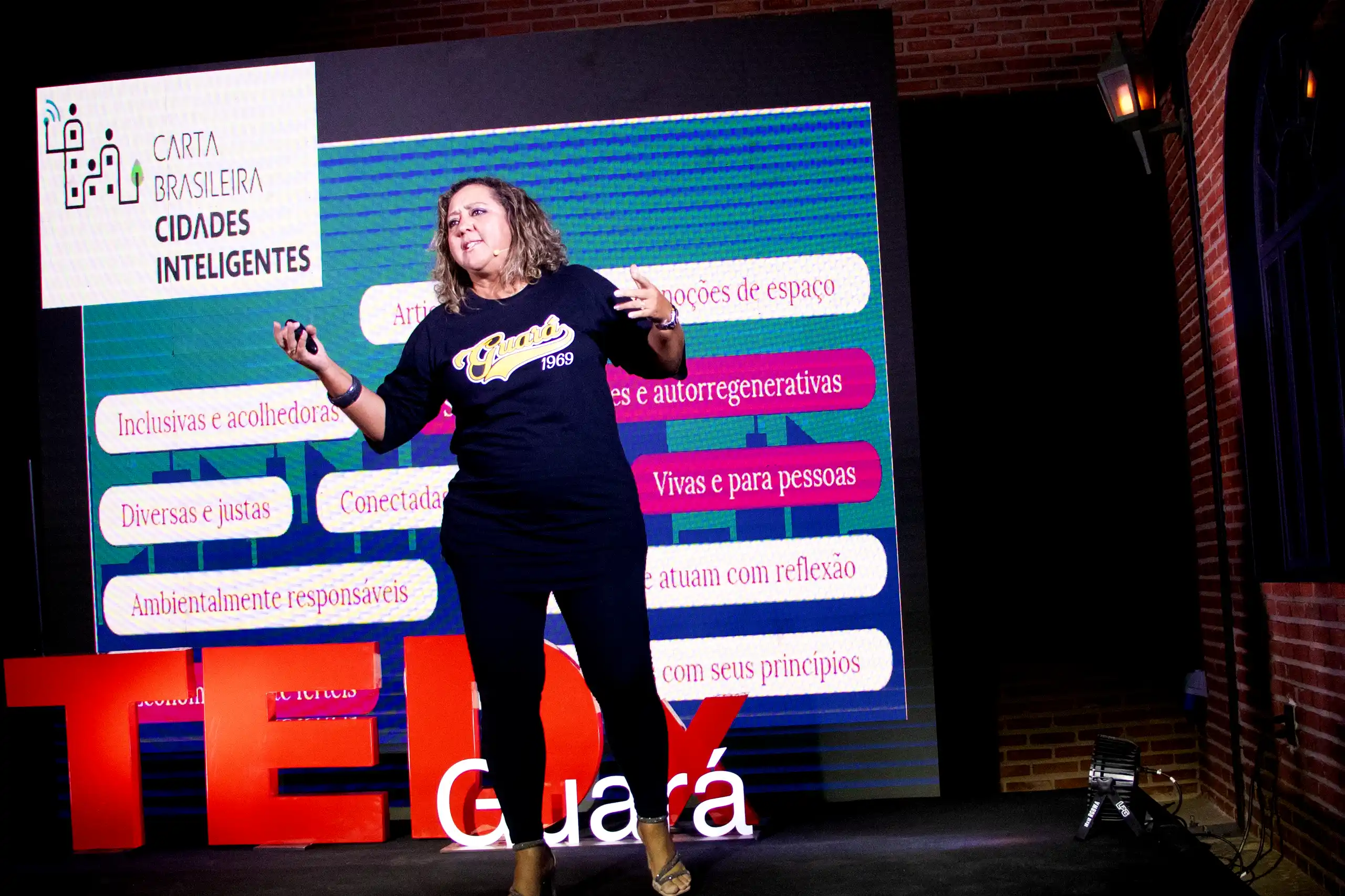 As contribuições de Cristiane junto à Carta Brasileira de Cidades Inteligentes A palestrante em uma entrevista recente para uma emissora de TV, explica como entrou no campo das cidades inteligentes contribuindo para o desenvolvimento da Carta Brasileira de Cidades Inteligentes, e posteriormente começou a trabalhar em projetos através do Instituto Multiplicidades. Um desses projetos, Hackacity Guará, visa implementar uma cidade inteligente em um bairro ou região específica, fornecendo oportunidades para a juventude local desenvolver ideias e negócios inovadores, e, finalmente, viver e trabalhar na cidade onde moram. O projeto, que é apoiado pelo Ministério da Ciência, Tecnologia e pela administração de Guará, com foco em educação, tecnologia e inserção no mercado para os jovens participantes tem sido uma referência em termos de políticas públicas aplicadas ao desenvolvimento de uma maneira de colaborar com os moradores da cidade. Entre algumas ações de sucesso no tema do empreendedorismo de inovação e promoção da economia digital e criativa, um Hackathon realizado na Faculdade Projeção, direcionou as ideias para os problemas reais da cidade e as três ideias empreendedoras de sucesso que ganharam a gincana receberam financiamento por meio de uma bolsa FAPDF, totalizando R$ 60.000 para saírem do papel. Uma dessas ideias foi a implementação de um posto de saúde em Guará, que visava gerenciar e distribuir medicamentos para a população local por meio de um aplicativo de celular. Outra ideia foi o desenvolvimento de um aplicativo para controlar e monitorar medicamentos dentro do posto de saúde. A palestrante também mencionou projetos em andamento, incluindo “Igualando Oportunidades”, que se concentra em inserir jovens negros no mercado de trabalho.
